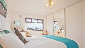 Une chambre avec un grand lit, une fenêtre donnant sur un beau paysage, un miroir et un luminaire au plafond.