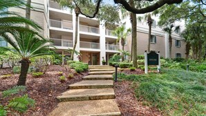 A multi-story building with a stone staircase leading to the entrance, surrounded by lush greenery and palm trees. - Cozy Villa, Pool View, Near Beach, So Many Amenities! Beach Wood (Fernandina Beach)