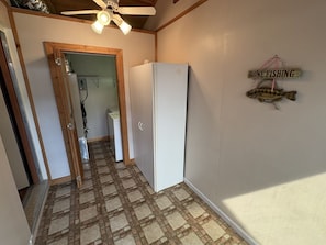 Corredor estreito com geladeira, ventilador de teto e uma placa com a inscrição 'Saúde para Pescar'.