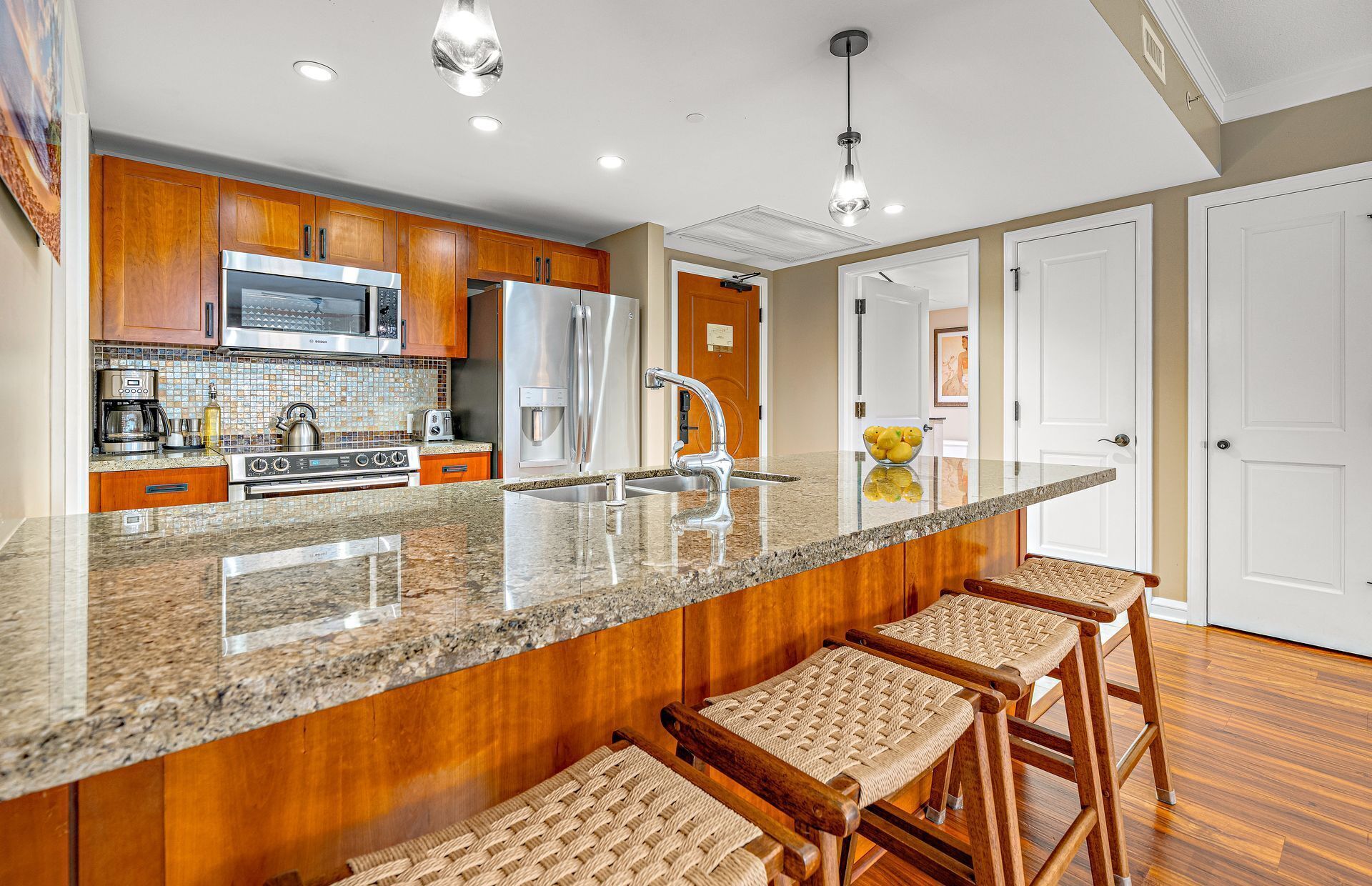 A modern kitchen with wooden cabinets, stainless steel appliances, a granite countertop, and bar stools.
