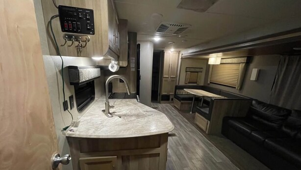 A compact kitchen with a marble countertop, wooden cabinets, and a built-in sink. - Come Settle in this cozy modern style RV, Nestled in the quiet country side. (Bushnell)
