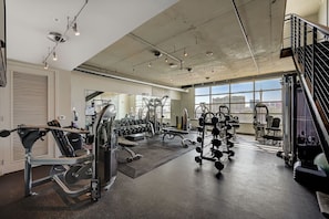 Ein Fitnessstudio mit unterschiedlichen Trainingsgeräten, großen Fenstern und Blick auf einen Turm.