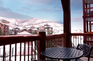 A balcony with a metal table and chairs, overlooking a snow-covered mountain and buildings. - Luxury 1-bedroom villa in tranquil Park City (Park City)