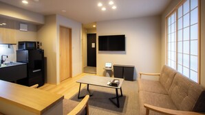 Una sala de estar moderna con un sofá, una mesa de centro, un televisor montado en la pared, una zona de cocina con microondas y una mesa de comedor de madera.