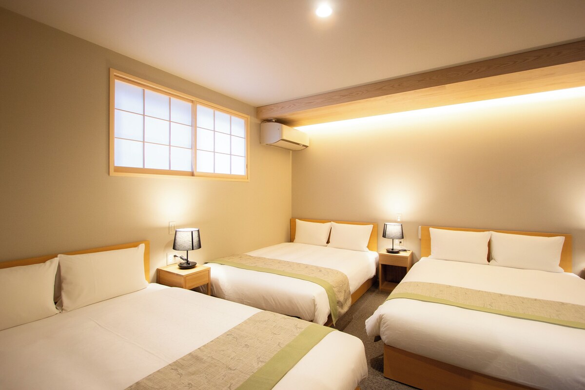 A hotel room with three beds, a large window, and an air conditioning unit.