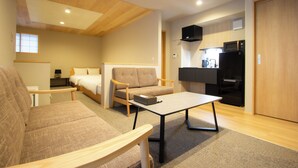Un espacio habitable moderno y compacto con sofá, una mesita, cama y kitchenette.