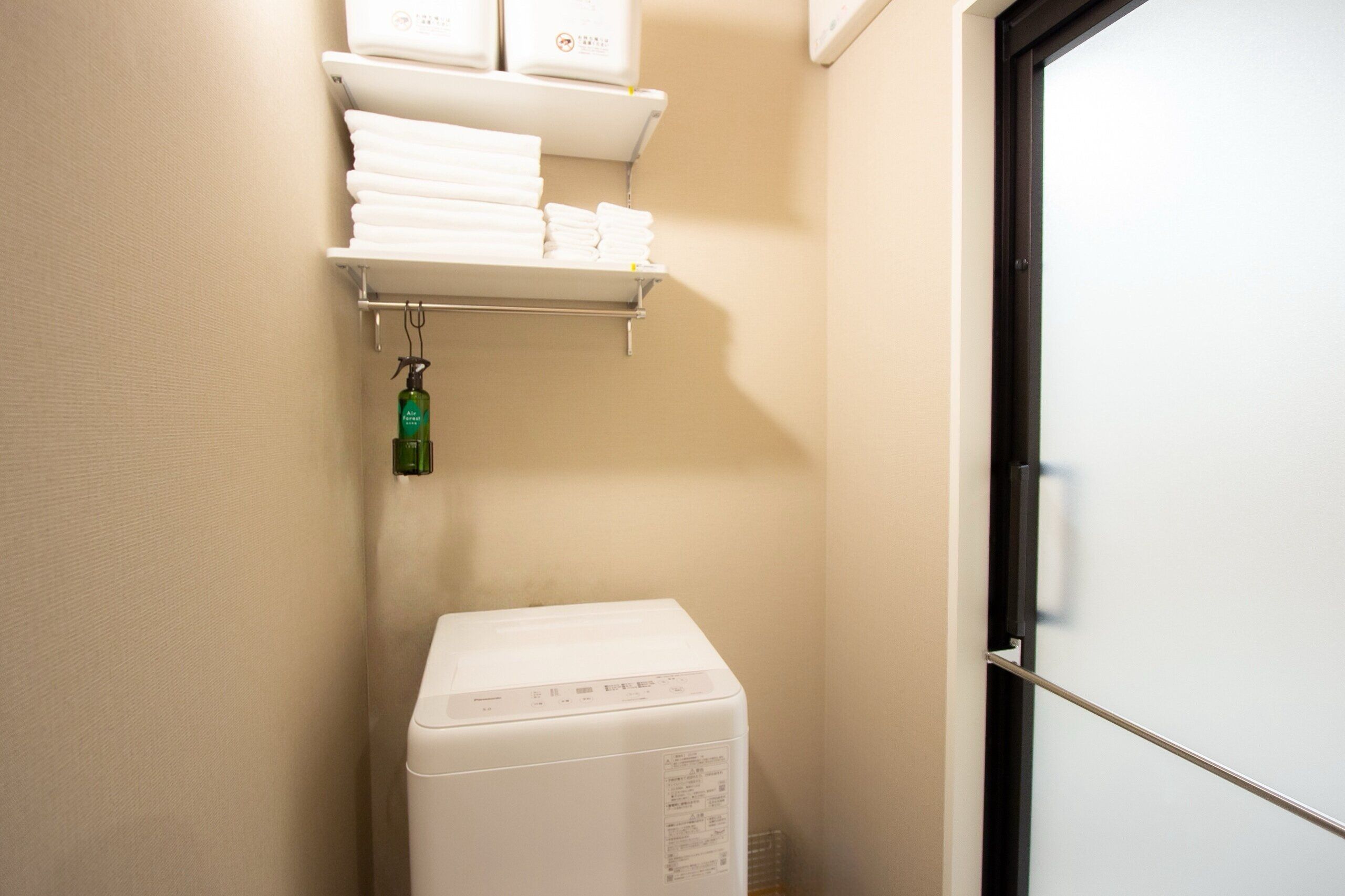 A laundry area with a washing machine, a shelf with folded towels, and a door.
