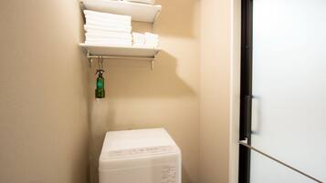 A laundry area with a washing machine, a shelf with folded towels, and a door.
