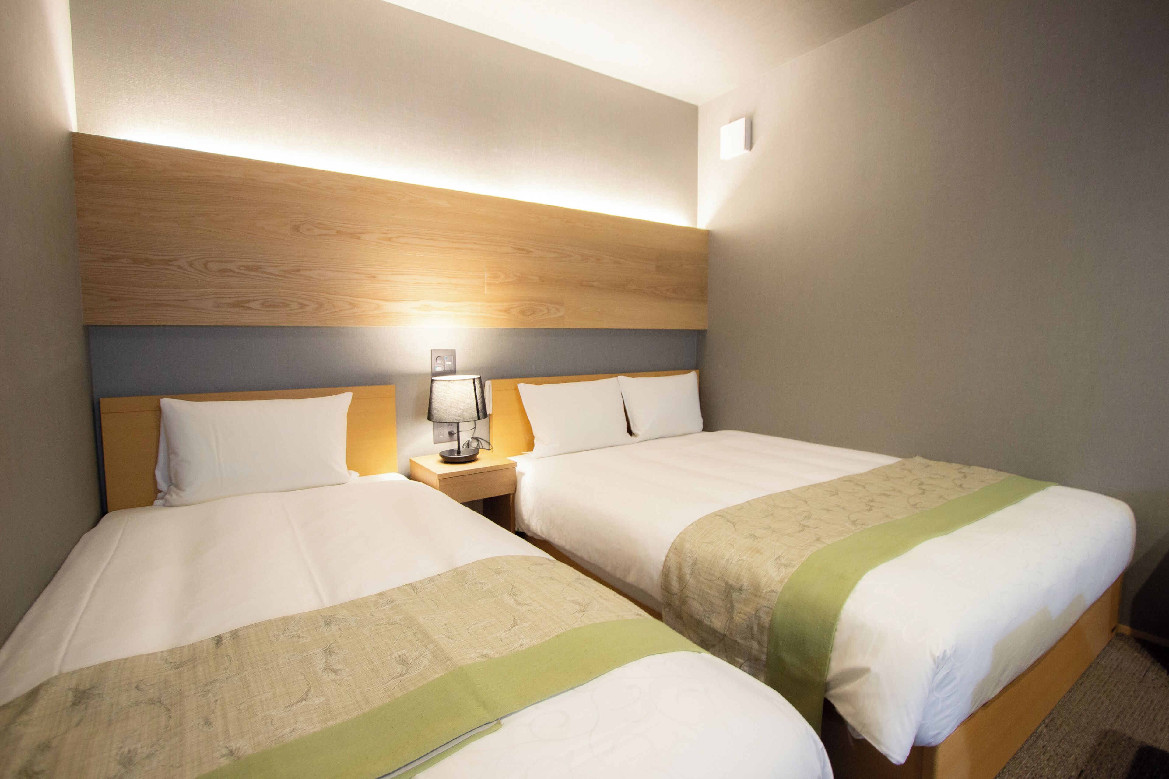 A hotel room with two beds, a nightstand with a lamp, and a wooden headboard.