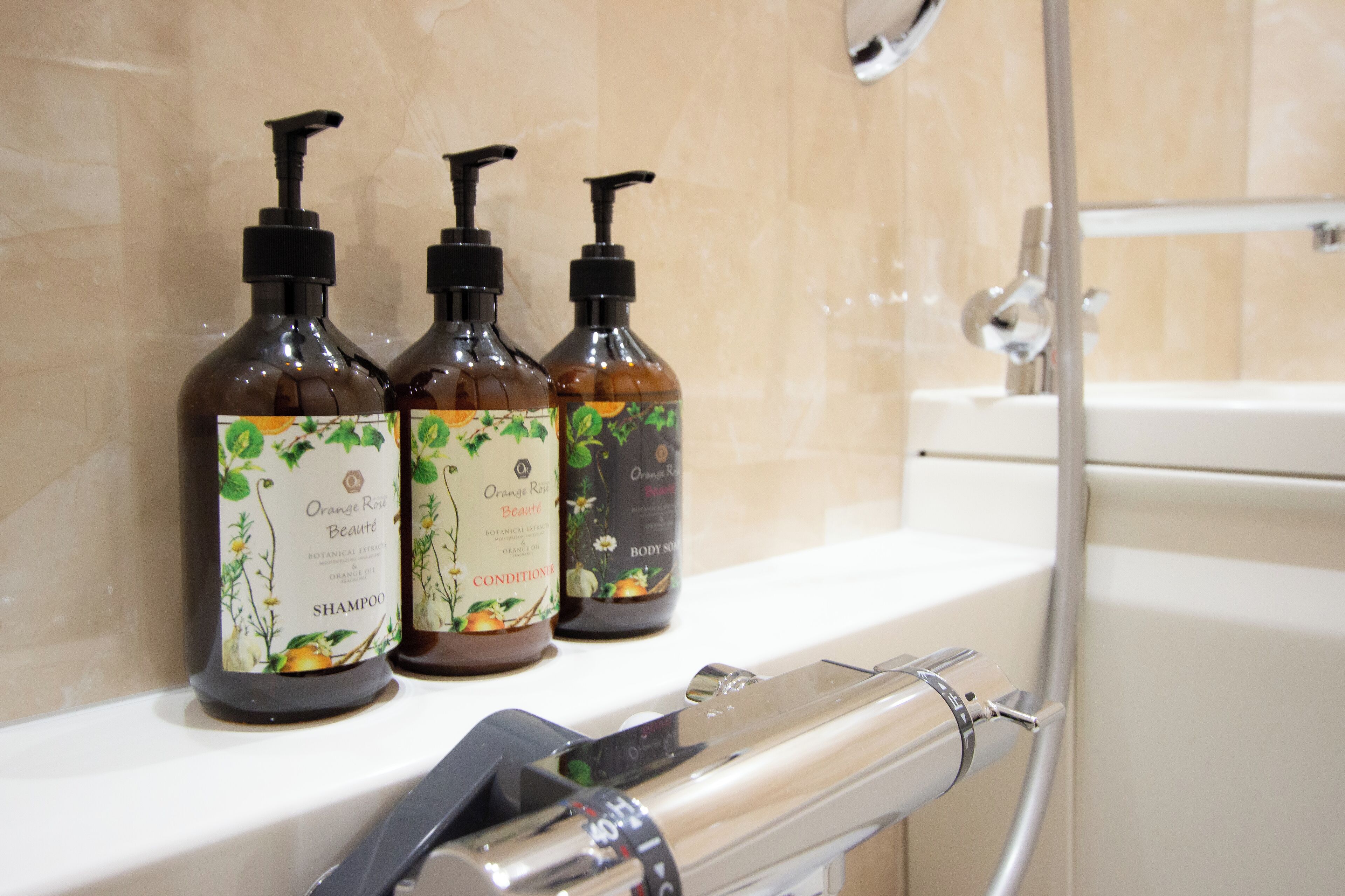Tres botellas de gel de ducha aroma naranja y rosa sobre una encimera de baño.