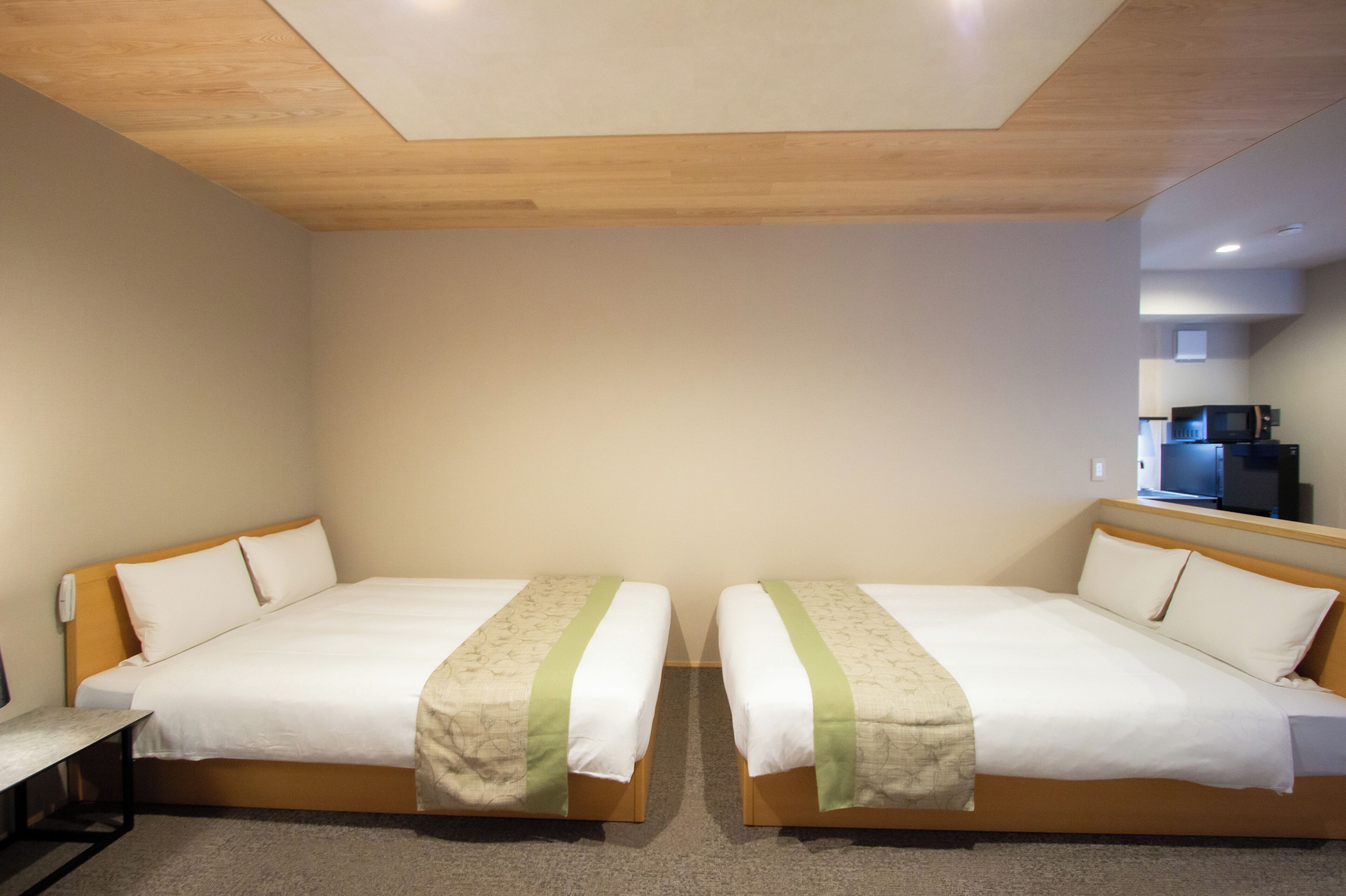 Habitación de hotel con dos camas, techo de madera, una pequeña cocina americana y un escritorio.
