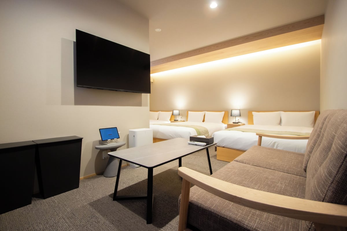A hotel room with a flat-screen TV, a desk with a computer, two beds, and a sofa.