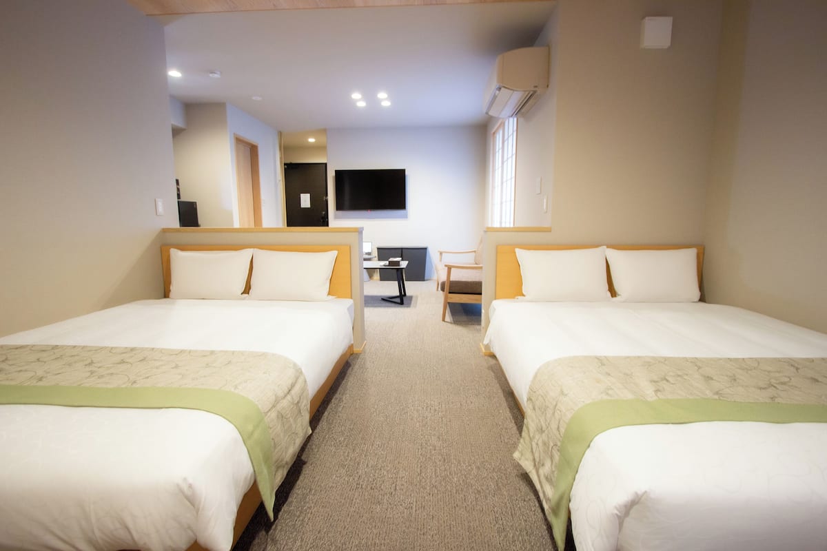 A hotel room with two beds, a desk, a chair, and a TV mounted on the wall.