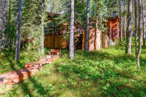 Une cabane en bois avec un escalier menant à l’entrée, entourée d’arbres.