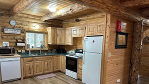 A log cabin kitchen with wooden cabinets, a white refrigerator, a stove, a microwave, and a dishwasher. - Hand Crafted Log Cabin in Island Park (Island Park)