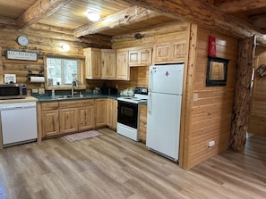 A log cabin kitchen with wooden cabinets, a white refrigerator, a stove, a microwave, and a dishwasher. - Hand Crafted Log Cabin in Island Park (Island Park)