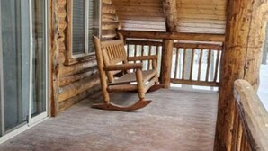 A wooden cabin with a porch, a rocking chair, and a table. - Hand Crafted Log Cabin in Island Park (Island Park)