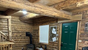 A log cabin interior with a wooden floor, a green door, a fireplace, and a small table with chairs. - Hand Crafted Log Cabin in Island Park (Island Park)
