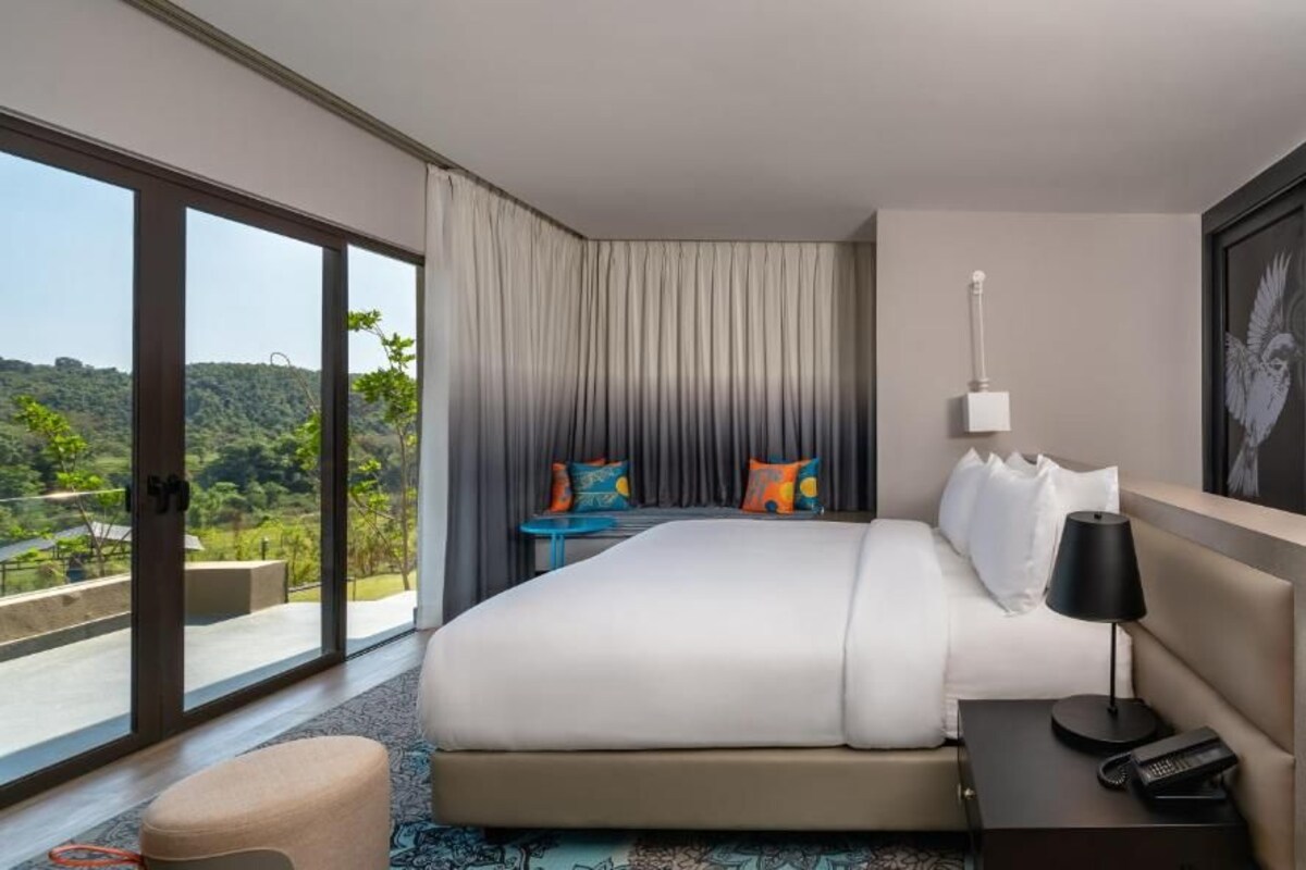 A hotel room with a large bed, a nightstand with a lamp, and a view of the outdoors.