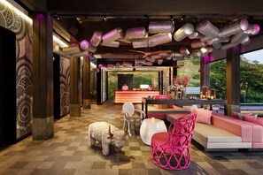 A modern interior with a checkered floor, a reception desk, a sofa, a pink chair, and a decorative sheep sculpture. - Norbu The Montanna, Dharamshala - Ihcl Seleqtions (Dharamshala)