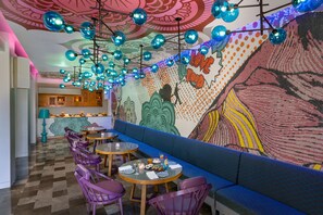 A restaurant with a patterned wall, blue and purple seating, and a ceiling with hanging blue spheres. - Norbu The Montanna, Dharamshala - Ihcl Seleqtions (Dharamshala)