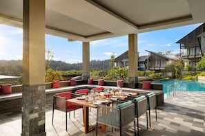 An outdoor dining area with a pool, stone pillars, and a view of the surrounding landscape. - Norbu The Montanna, Dharamshala - Ihcl Seleqtions (Dharamshala)