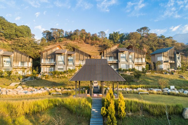 Un resort moderno con varias construcciones, un pabellón central y un paisaje natural en la ladera de una colina.
