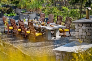 An outdoor dining area with a stone table and wooden chairs, surrounded by greenery and a stone wall. - Norbu The Montanna, Dharamshala - Ihcl Seleqtions (Dharamshala)