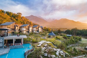Un resort con varias construcciones, piscina y montañas al fondo.