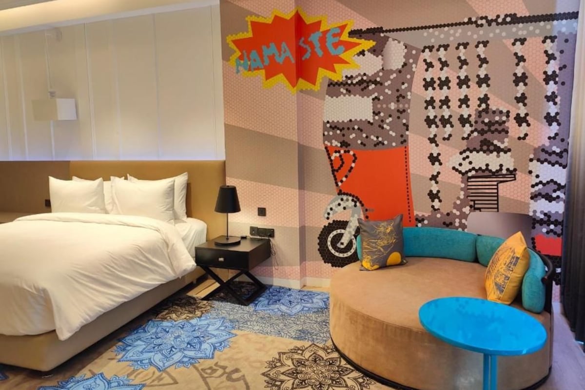 A modern hotel room with a bed, a seating area, and a wall with a colorful abstract design.
