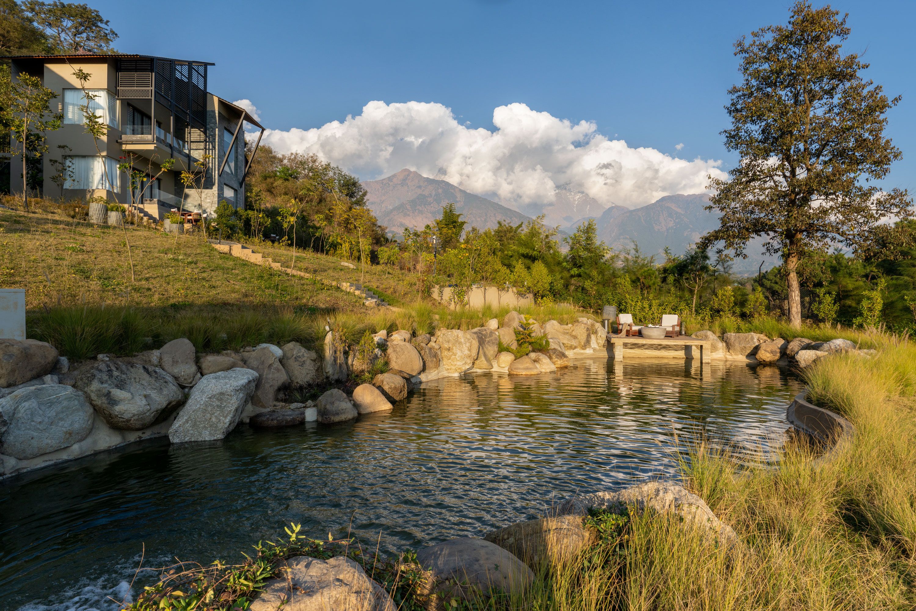 A modern house with a large water feature, a stone pathway, and a mountain backdrop.