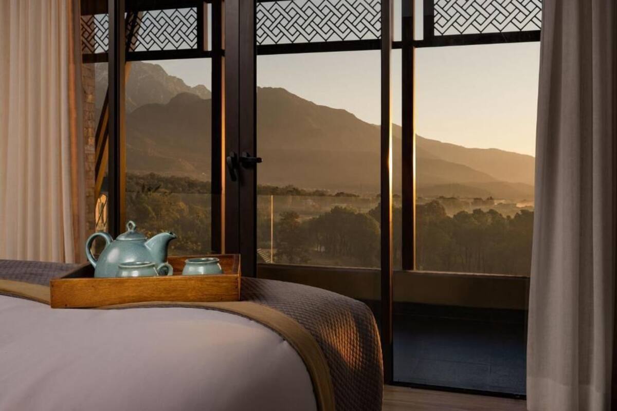 Ein Schlafzimmer mit großem Fenster, einem Bett, einem Holftablett mit Teekanne und Tassen sowie Blick auf Berge.