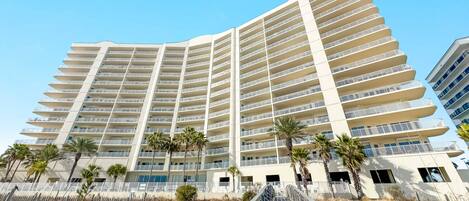 Un hotel de varios pisos con balcones, palmeras y una escalera que lleva a la entrada.
