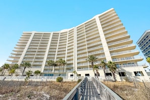 Ein mehrstöckiges Hotel mit Balkonen, Palmen und einer Treppe, die zum Eingang führt.