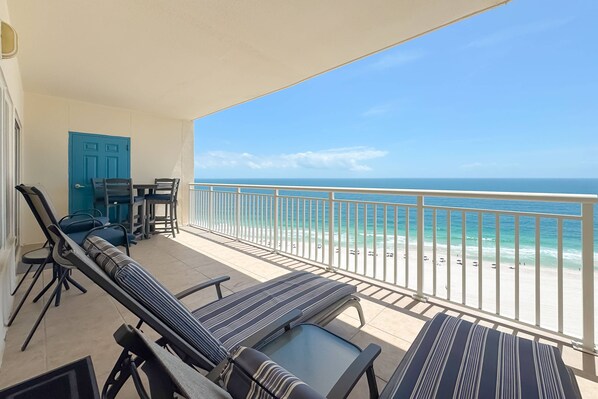 Ein Balkon mit Liegestühlen, einem Tisch und Stühlen mit Blick auf einen Strand und freien Blick auf das Meer.
