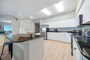 A modern kitchen with white cabinets, a black countertop, and a central island. - Admirals Quarters 1504 | Gulf-Front + Hot Tub (Orange Beach)