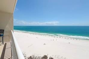 Blick auf einen Strand vom Balkon mit Geländer, einem klaren Himmel und dem Meer.