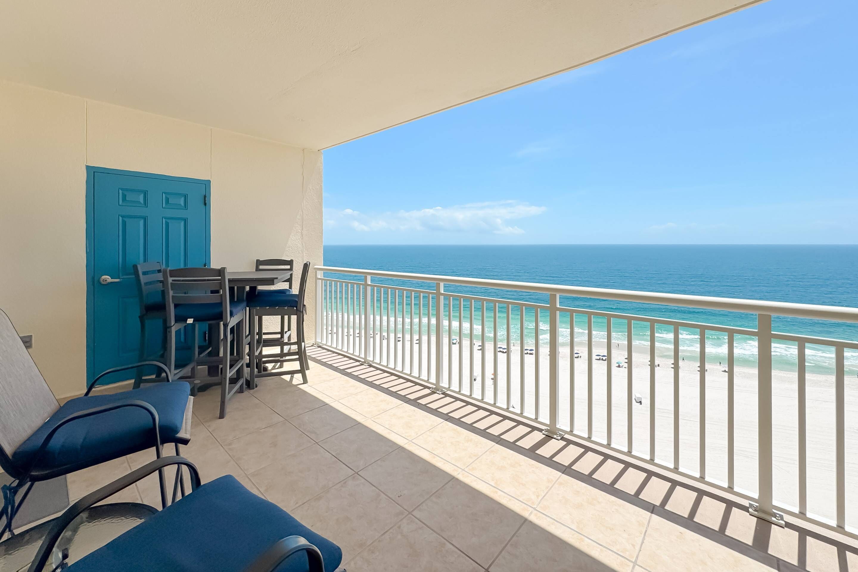 Un balcon avec vue sur l’océan, une porte bleue et une table avec des chaises.