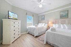 A bedroom with two beds, a dresser, a ceiling fan, and artwork on the walls. - Admirals Quarters 1504 | Gulf-Front + Hot Tub (Orange Beach)