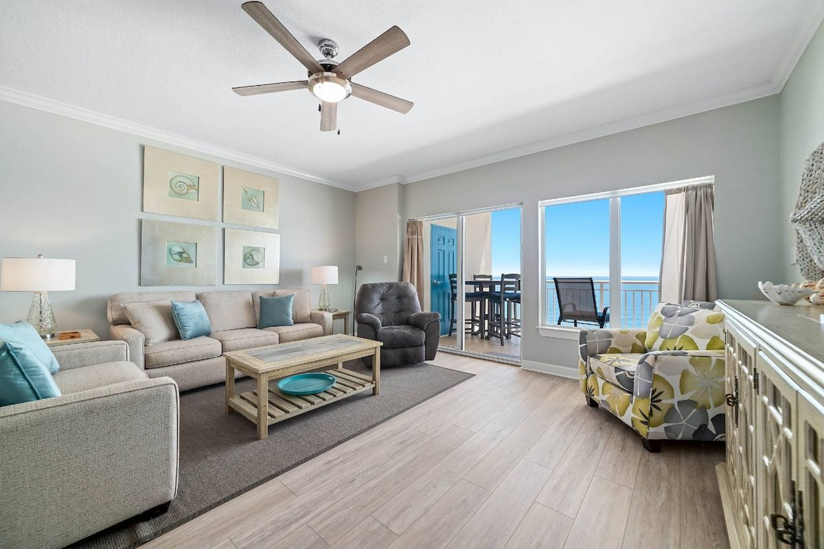 A spacious living room with a ceiling fan, a sofa set, a coffee table, and a view to the outside.