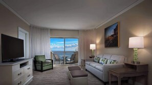 A hotel room with a television, a green armchair, a sofa with patterned cushions, a small table, and a painting on the wall. - Marriott's OceanWatch | Oceanfront 2 BR Villa (Myrtle Beach)