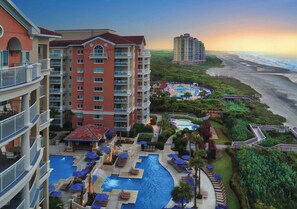 A hotel with multiple floors, a pool area with sun loungers, and a view of the beach. - Marriott's OceanWatch | Oceanfront 2 BR Villa (Myrtle Beach)