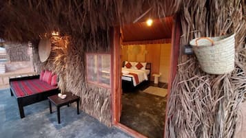 A thatched-roof room with a bed, a small table, and a bench.