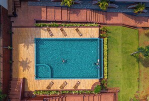 An aerial view of a rectangular swimming pool with wooden deck and lounge chairs, surrounded by a grassy area and a brick wall. - Zo Selections Gokarna by Zostel (Gokarna)