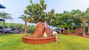 A garden with a large rock formation and a statue, surrounded by lush greenery and palm trees. - Zo Selections Gokarna by Zostel (Gokarna)