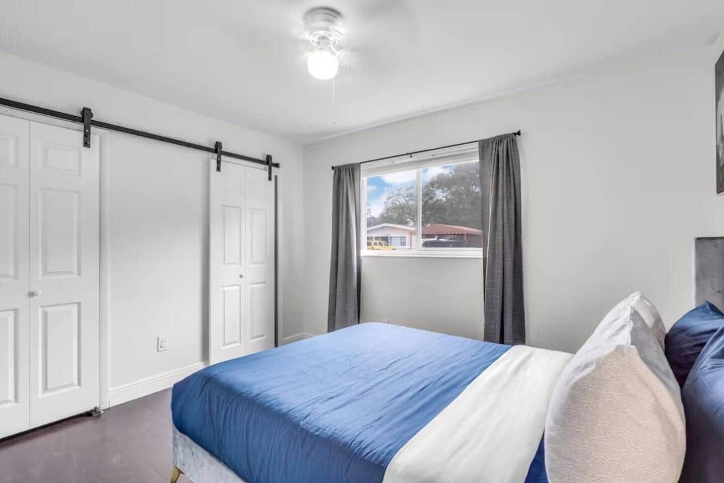 Ein Schlafzimmer mit einem Bett, einem Fenster mit Vorhängen und einem Deckenventilator.