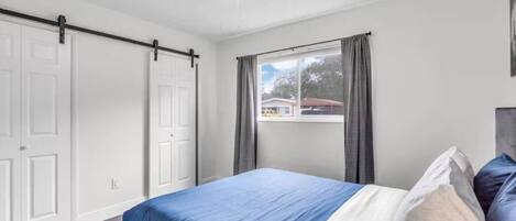 Ein Schlafzimmer mit einem Bett, einem Fenster mit Vorhängen und einem Deckenventilator.