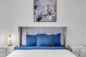 A modern bedroom with a tufted headboard, a large bed with blue bedding, and a bedside table with a lamp. - Luxury 4bd 2bath With Pool and Grill in Miami! (Miami)