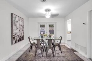 A dining area with a glass table and chairs, a ceiling fan, and a large abstract painting on the wall. - Luxury 4bd 2bath With Pool and Grill in Miami! (Miami)