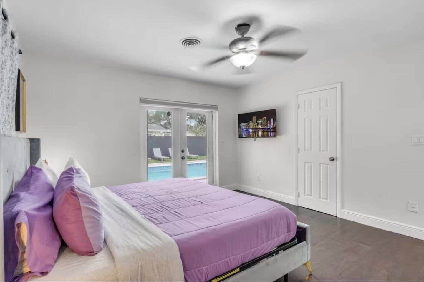 A bedroom with a bed, a ceiling fan, a door, and a view of a pool.
